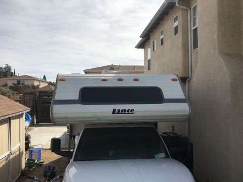 1997 Dodge 3500 - A white truck is parked next to a building, with a Lance camper installed.