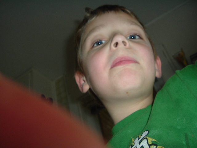 Kid looking up at the camera, wearing a green shirt. Text on shirt says SUPERMOTORS