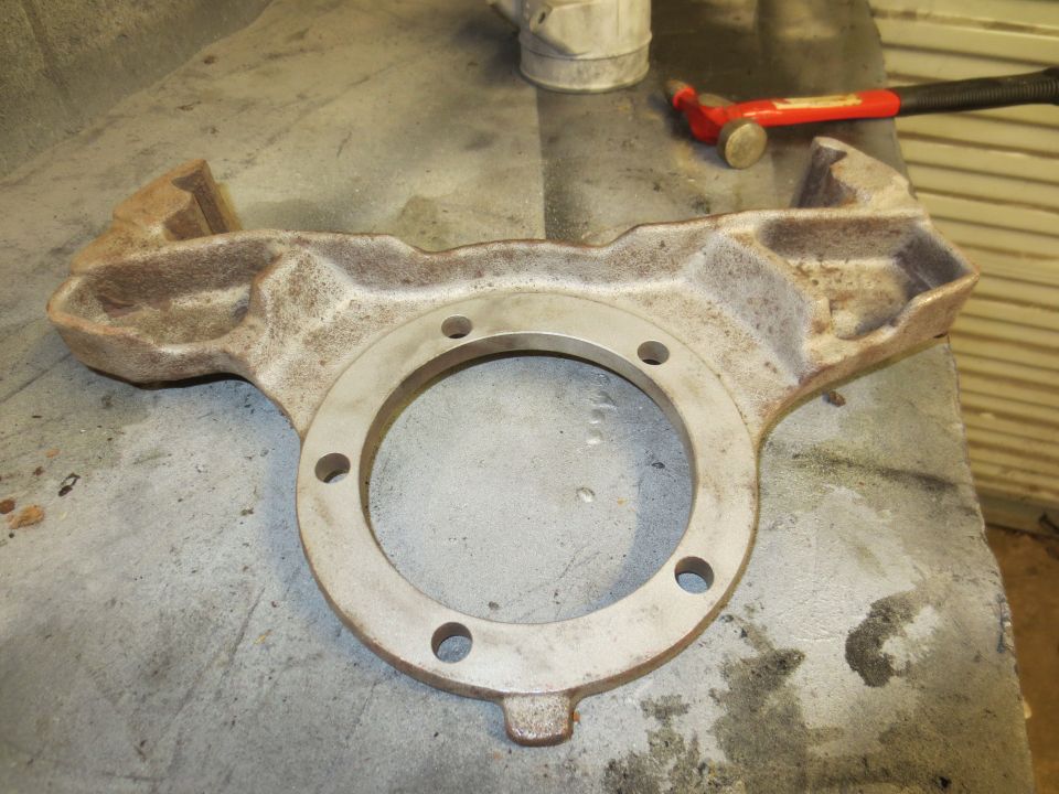 Cast iron part with a circular opening and bolt holes, sitting on a workbench. A hammer is visible in the background