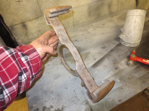1967 Ford F-250 - A hand holds a rusty metal tool with a circular opening and two flat ends, with a hammer and a metal container in the background.
