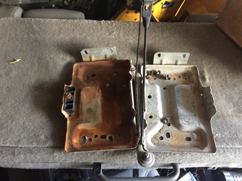 1996 Ford Bronco - Comparison of two battery trays, one showing significant rust and the other appearing in better condition.