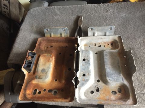 1996 Ford Bronco - Comparison of a rusty and a clean dual battery tray, possibly for a vehicle.