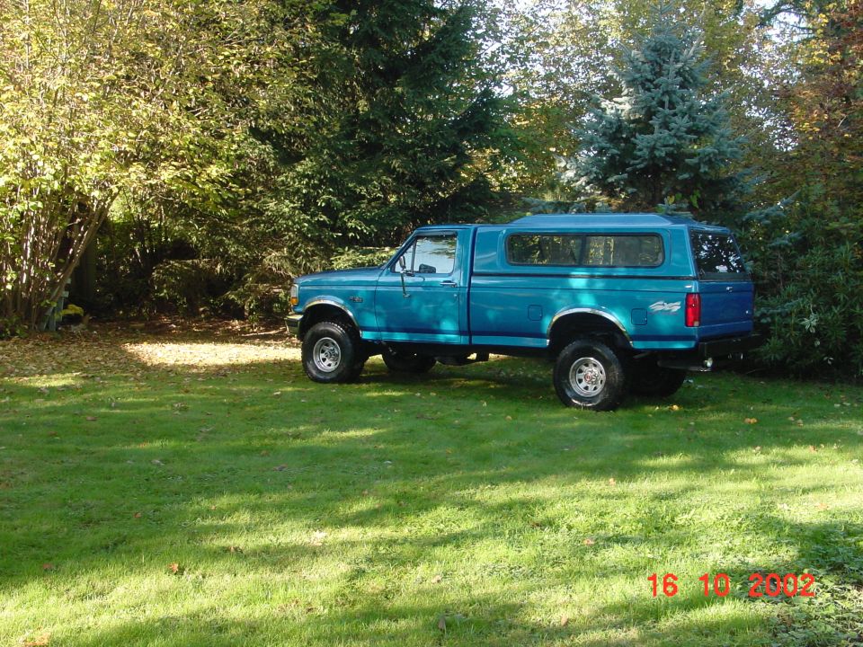 1992 Ford F-150 pickup truck, blue, with a blue camper shell, parked on grass with trees in background