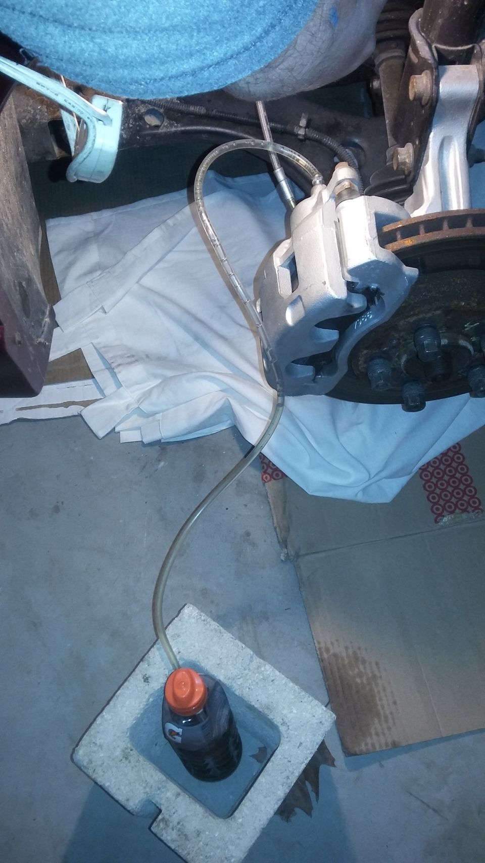 Brake caliper with bleed tube draining fluid into bottle on concrete floor