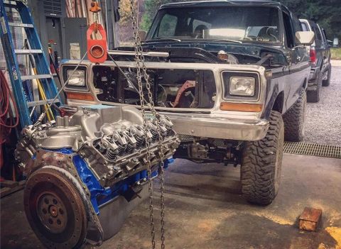 1979 Ford Bronco - A Ford Bronco is in a garage with its engine being removed by a hoist, and another vehicle is parked behind it.