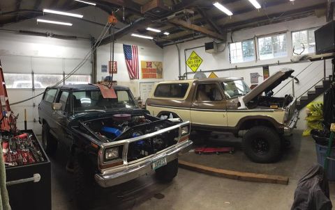 1979 Ford Bronco - Two Ford Broncos are parked in a garage, both with their hoods open for maintenance.