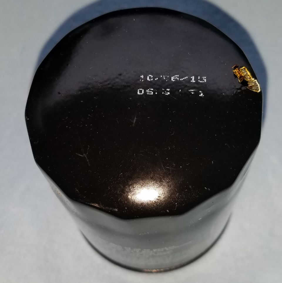 Black oil filter with stamped date 10.16.15 and time 08:31, with a small gold-colored piece of debris on top