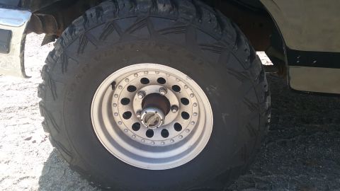 1993 Ford Bronco - Close-up of a 1993 Ford Bronco's front wheel and tire, showing the silver alloy rim and a portion of the vehicle's body.
