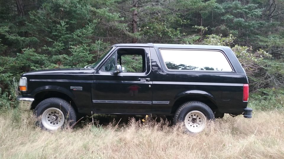 Side view of a black 1993 Ford Bronco parked in tall grass and trees