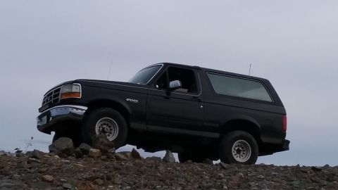 1993 Ford Bronco - A black 1993 Ford Bronco is positioned on a rocky incline with a muted sky in the background.