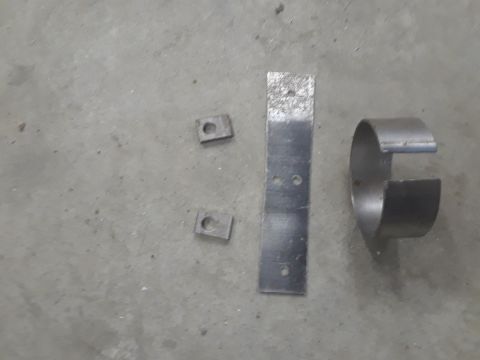 1985 Ford Bronco - Several metal parts, including brackets and a clamp, are laid out on a concrete floor.