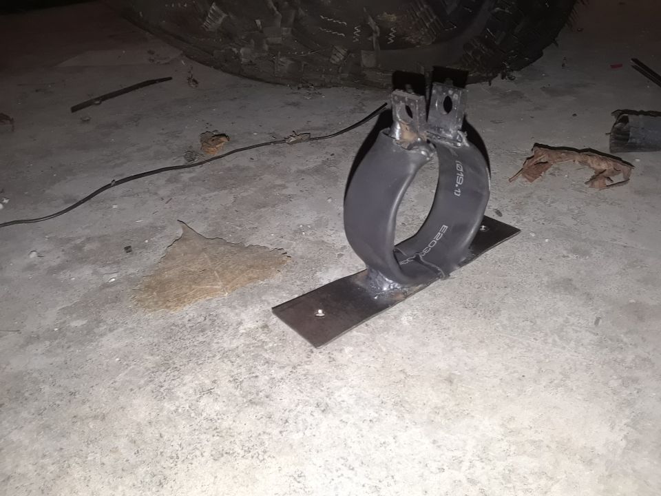 Custom exhaust hanger made from a rubber hose and metal brackets, sitting on a concrete floor next to a tire
