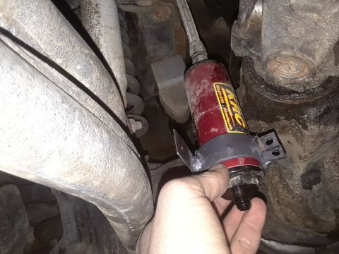1985 Ford Bronco - A hand holds a red fuel filter with a yellow label, part of a vehicle's fuel system.