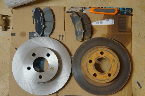 1998 Ford Ranger - A new brake rotor sits next to a rusty old one, with new and used brake pads nearby.