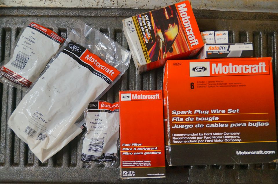 Several Motorcraft auto parts, including spark plug wire set, oil filter, and fuel filter, laid out on a truck bed