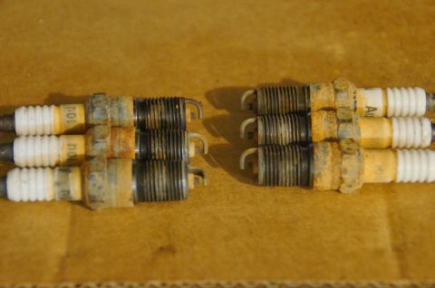 1998 Ford Ranger - Six used spark plugs are laid out on a brown surface. Some show signs of wear and rust.