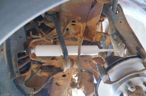 1998 Ford Ranger - Close-up view of suspension parts, highlighting a newly installed white shock absorber against a backdrop of rust and grime.