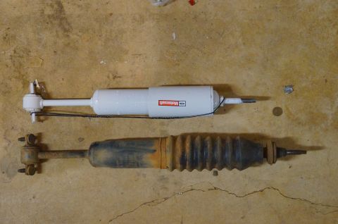 1998 Ford Ranger - Two shock absorbers are laid out on a concrete surface, one new and one old and corroded.