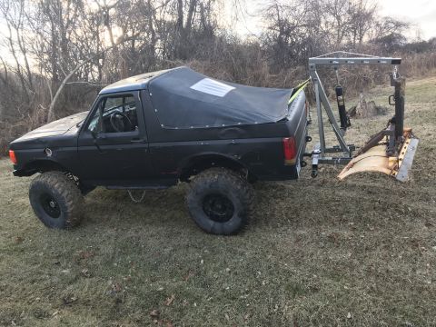 1989 Ford Bronco - This modified Ford Bronco is equipped with a plow attachment, suggesting it's prepared for snow removal or land clearing.