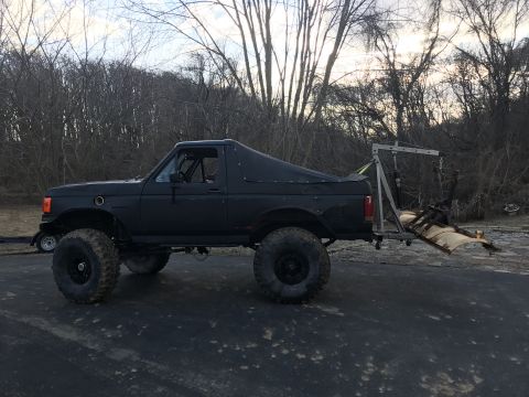 1989 Ford Bronco - Side view of a modified 1989 Ford Bronco, equipped with oversized tires and a soft top cover.