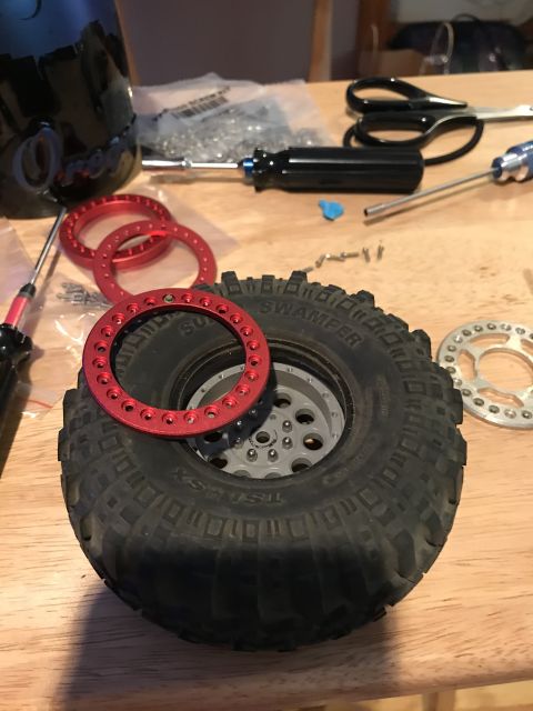 1989 Ford Bronco - A close-up view shows a RC car tire and wheel assembly with red beadlock rings and a silver beadlock ring. Tools and hardware are scattered…