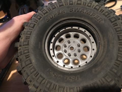 1989 Ford Bronco - A close-up view of a "Super Swamper" tire with a silver beadlock wheel. The tire has aggressive tread patterns and visible text on its side…