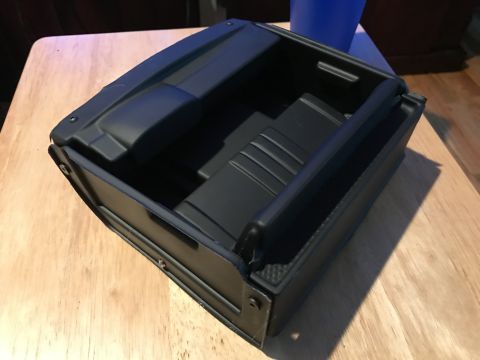 1989 Ford Bronco - A black plastic center console storage compartment is shown from a high angle, resting on a wooden surface.