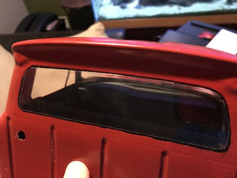 1989 Ford Bronco - Close-up of the rear window and bed of a red pickup truck. The window is blacked out and framed by the red body, with visible panel lines o…