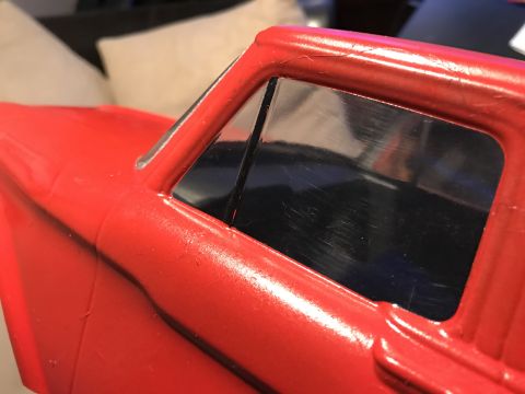 1989 Ford Bronco - Close-up view of the driver's side window frame and the triangular vent window on a red vehicle. The paint shows some wear and tear, with m…