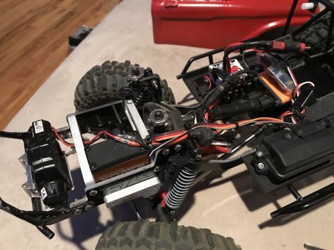 1989 Ford Bronco - Close-up, overhead view of the chassis and electronics of a remote-controlled rock crawler. Visible parts include a black motor, silver ser…