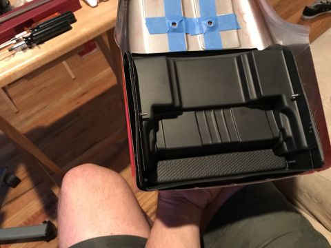 1989 Ford Bronco - A person holds a black plastic interior component, possibly a battery box, with a metallic silver exterior shell attached to it. The compon…