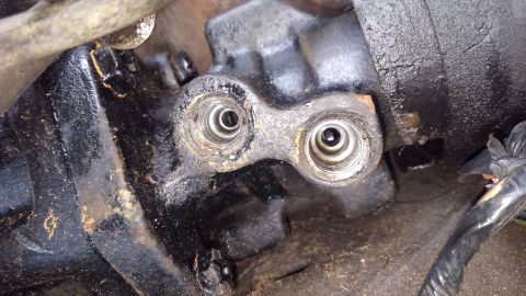 1988 Ford Bronco - A close-up view shows two threaded openings on a greasy, black metal component, likely part of an engine or transmission. The openings have…