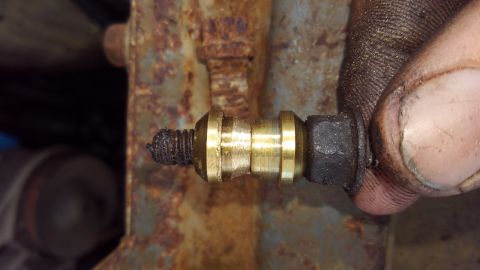 1988 Ford Bronco - A close-up view shows a brass fitting with a threaded end covered in grease, attached to a rusty metal bracket. A person's dirty thumb and…
