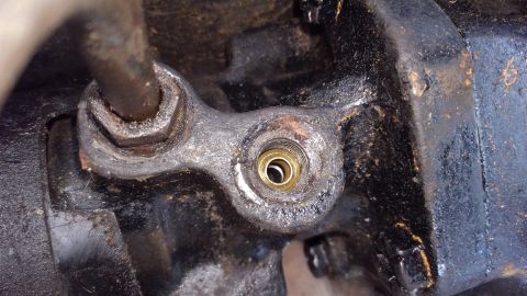 1988 Ford Bronco - A close-up view shows a brass fitting with visible threads, likely part of a hydraulic or fluid system, attached to a black, greasy metal c…