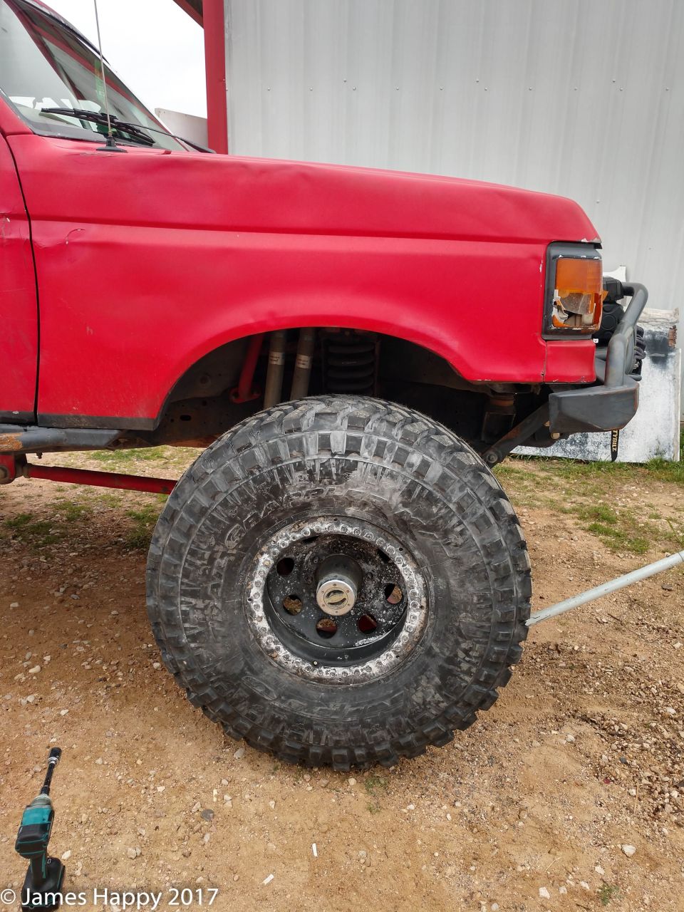 Red Ford Bronco front fender and large off-road tire, with impact wrench on ground.