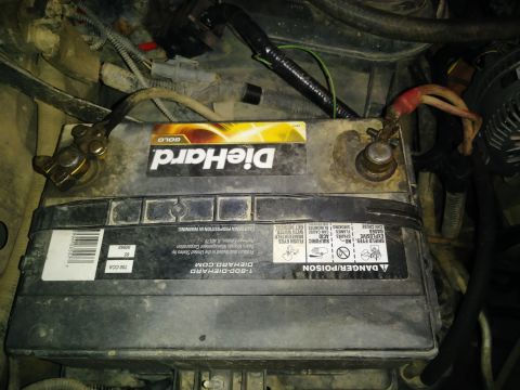 1996 Ford Bronco - A DieHard Gold car battery is shown installed in an engine bay, with red and black battery cables connected to the terminals. The battery h…