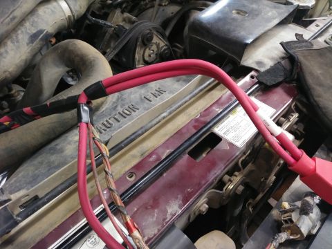 1996 Ford Bronco - Close-up view of red battery cables connected to a vehicle's engine bay, with black electrical tape securing the connections. Visible text…