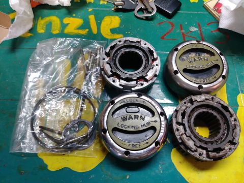 1996 Ford Bronco - Four Warn locking hubs and a bag of assorted parts are laid out on a green surface with yellow markings. Two of the hubs are labeled "WARN…