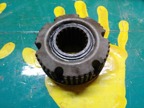 1996 Ford Bronco - A close-up of a metal gear with internal splines rests on a teal surface with yellow handprint markings. The gear appears to be a component…