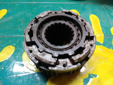1996 Ford Bronco - A close-up, overhead view of a heavily used, dirty metal automotive part with internal splines and external teeth. The part is resting on a…