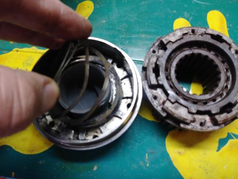 1996 Ford Bronco - A hand holds a disassembled metal component with internal springs, next to another similar component with splines. The parts are on a green…