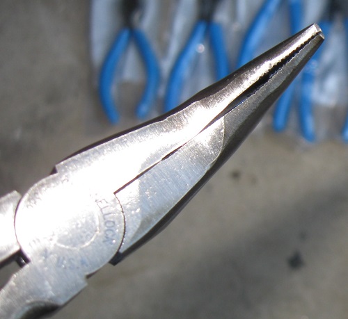 Close-up of needle-nose pliers with blue-handled pliers in the background.