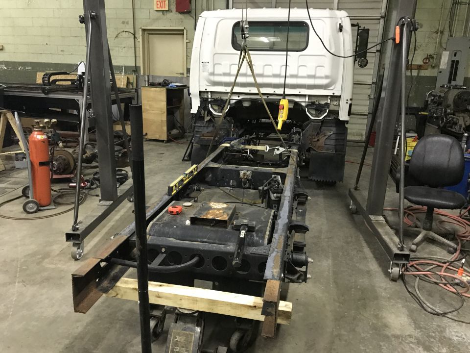 White truck cab suspended over bare chassis in a garage.