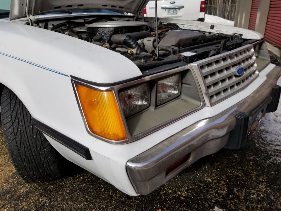 Photo of a white Ford front end with open hood and headlights