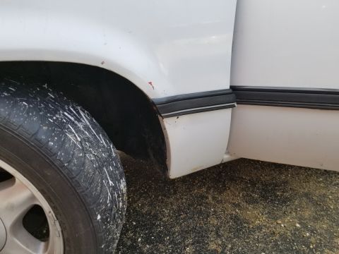 2001 Ford Crown Victoria - Photograph of a white truck's rear wheel arch and rocker area with surface rust; not a technical document.