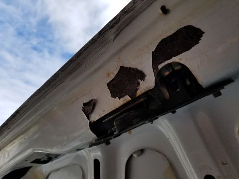 2001 Ford Crown Victoria - Photograph of a rusty upper body panel seam and hinge bracket; not a technical document.