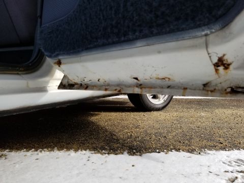 2001 Ford Crown Victoria - Photograph of a rusted rocker panel beneath an open car door; not a technical document.