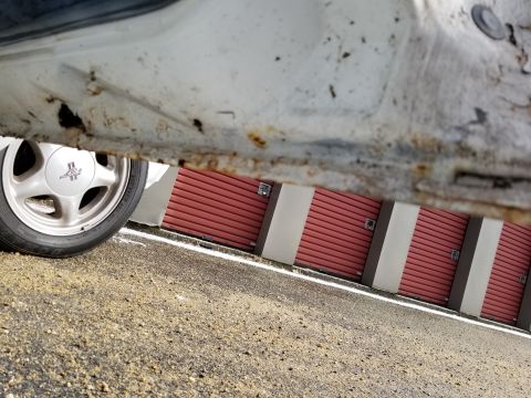 2001 Ford Crown Victoria - Photograph of a corroded rocker panel and wheel beside a red wall; not a technical document.