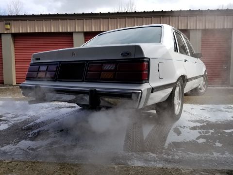 2001 Ford Crown Victoria - Photo of the rear of a white Ford LTD sedan with exhaust smoke, not a technical document.