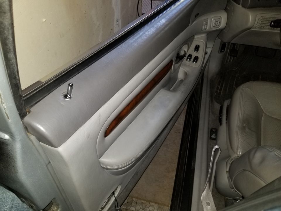 Close-up of a car's gray leather door panel with wood trim and lock pin.